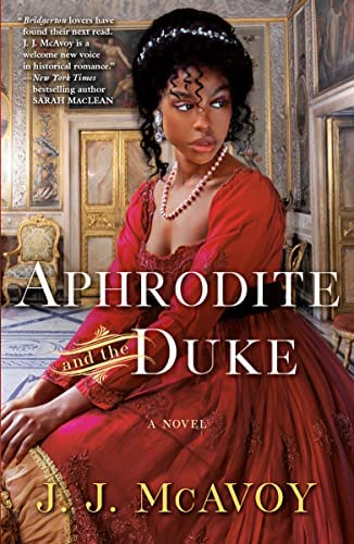 Aphrodite and the Duke by J.J. McAvoy. A Black woman in a gorgeous red dress sitting in an ivory and gold ballroom. Her curly hair is piled atop her head and she's wearing a pearl necklace and gemstone headband.