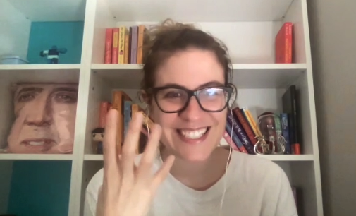 Ali Hazelwood holding up four fingers on our zoom call with a bookshelf behind her including a Nicholas Cage pillow that fits PERFECTLY on the shelf 