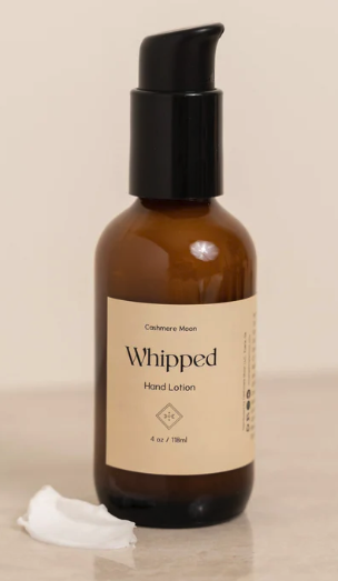 Cashmere Moon whipped hand lotion in a brown bottle with a black pump top on a beige marble background