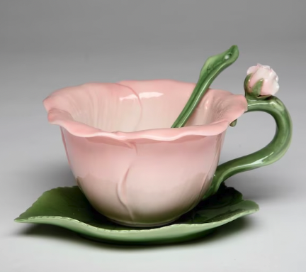 A pink teacup shaped to look like a hibiscus flower with a green leaf saucer and a tiny green leaf shaped spoon