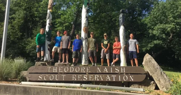 Color photo of scouts standing on a sign that reads Theodore Naish Scout Reservation