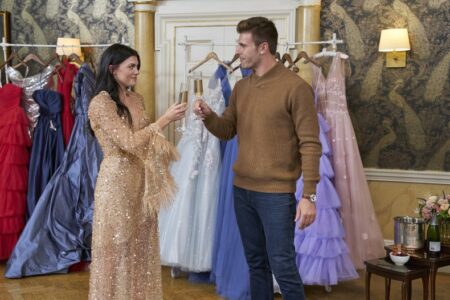 Gabi and Zach toast champagne in front of a rack of gowns