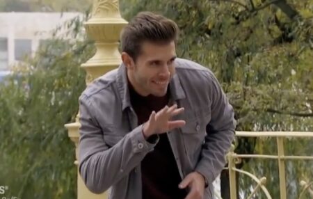 Zach crouches down and does a little finger wave while grinning like someone who absolutely wants to eat your face