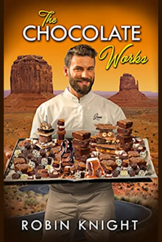 The Chocolate Works by Robin Knight. A man in a white chef's jacket holds a platter of chocolate and brownies while he smiles. Behind him is a desert with two large mesas. 