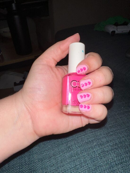 Amanda's hand holding a bottle of hot pink nail polish. her nails are light pink with dark ping lines of hearts in a row on each - they're adorable