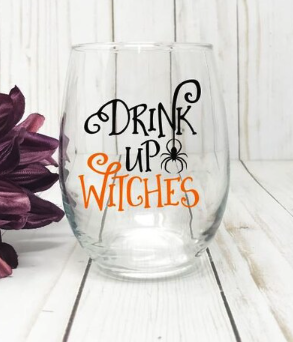 A stemless wine glass with DRINK UP WITCHES written in orange and black curly letters with a tiny spider hanging from the K in DRINK 