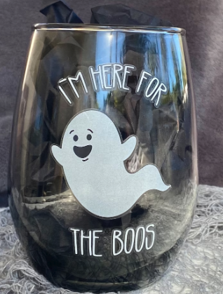 A grey shaded wine glass with no stem with a happy ghost on the front that reads I'm HERE For the BOOS 