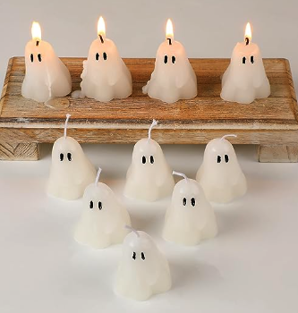2-inch tall ghost cnadles with little black eyes and wicks on their head. four of them are lit and on a wooden shelf while six are in a pyramid arrangement in front they're so cute 