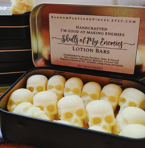 a metal tin of molded skull lotion and soaps with a label on the lid that says Hand crafted: I'm good at making enemies SKULLS OF MY ENEMIES Lotion Bars 