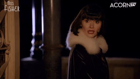 Phryne Fisher from Miss Fisher's Mysteries wearing a white fur collar and a black coat hoists a small gun with a big smile