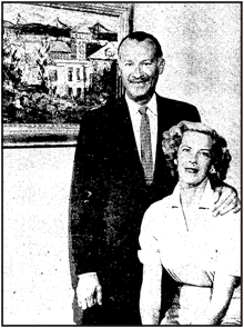 a black and white grainy photo of a white man wearing a tie with a small mustache maybe and a woman with light hair in 50s curls in a white blouse seated in front of him and he has his hand on her shoulder