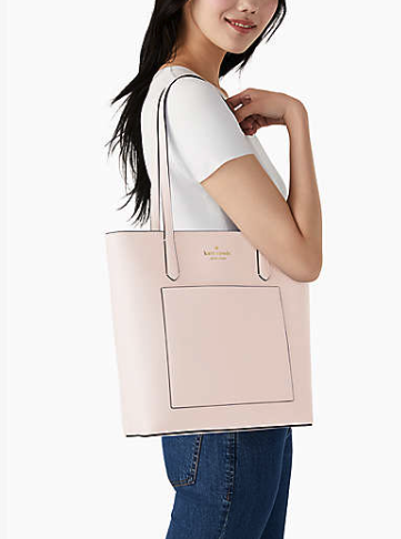 A side view of a woman with long dark hair holding the bag. it goes over the shoulder and is roomy enough that the bottom is below her waistline