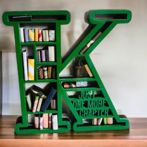 A green K with tiny shelves inside, each with different miniature books in colored paper, and in the lower right corner it says JUST ONE MORE CHAPTER