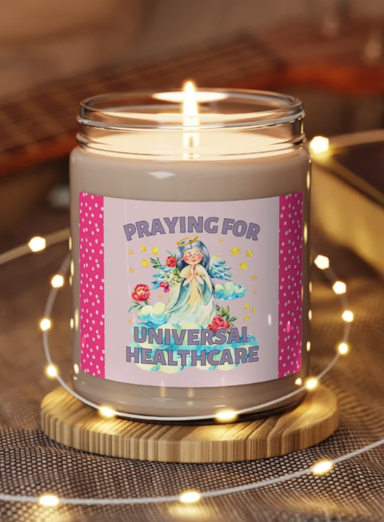A jar candle with an illustration of a small angel with blue hair and text that reads praying for universal health care