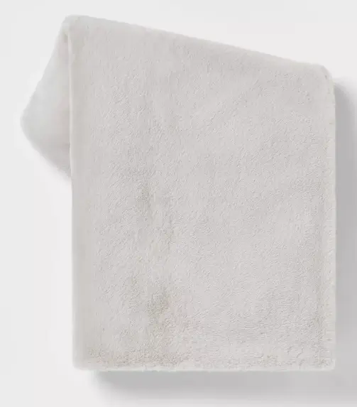 A grey faux fur folded blanket against a grey background 