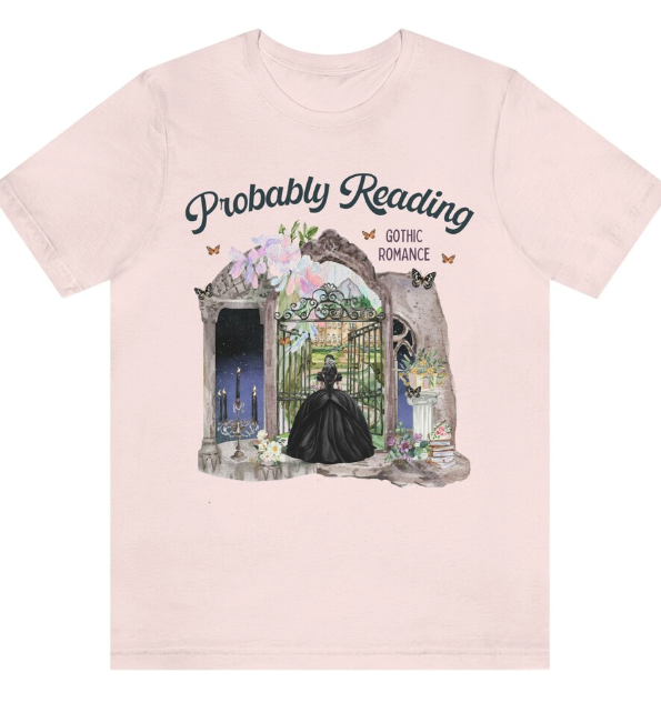 A pink t shirt with an illustration of a dark dressed woman opening an iron gate with a candelabra and stone scrolls around her and the words probably reading gothic romance 