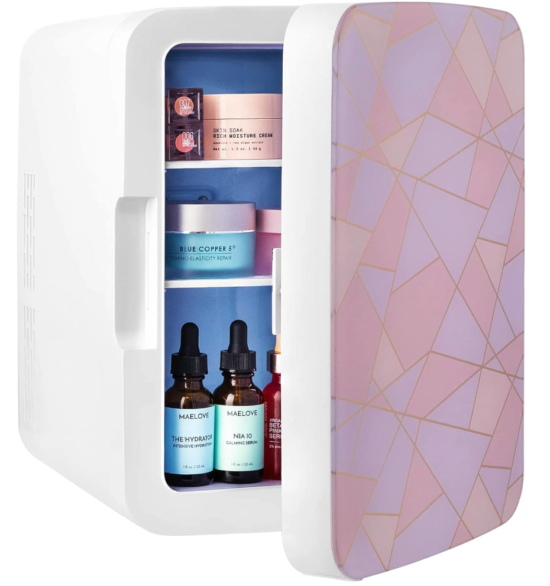 A small countertop fridge with a pink geometric pattern on the front with gold lines. The door is partially open so you can see bottles and pots of skincare inside
