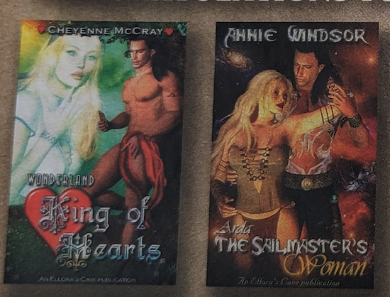 An image of two Ellora's Cave covers. King of Hearts by Cheyenne McCray features a computer generated Poser image of a very pale white woman with wide eyes and her finger touching her chin with her hand splayed open as she gazes at a shirtless naked man with a red scarf over his bits Arda the Sailmaster's woman by Annie Windsor is a blonde Poser Computer generated White woman with long white hair, red lips and a lace up top barely containing her extremely large and round breasts dancing I think? With a dark haired shirtless White guy with black pants and a massive belt it's very weird they look like they are doing a tango in space except her arm is bent and reaching up behind his neck but with the angle her arm is about nine yards long