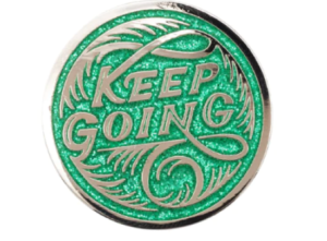 Keep Going in stylized loopy script against a green glitter enamel background on a round disk pin