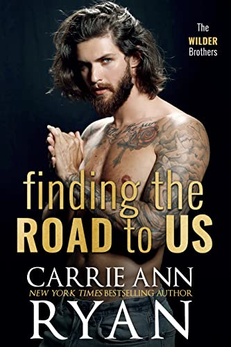 Find the Road to Us by Carrie Ann Ryan. A shirtless man with long, brown hair and chest tattoos is cupping his palms together.