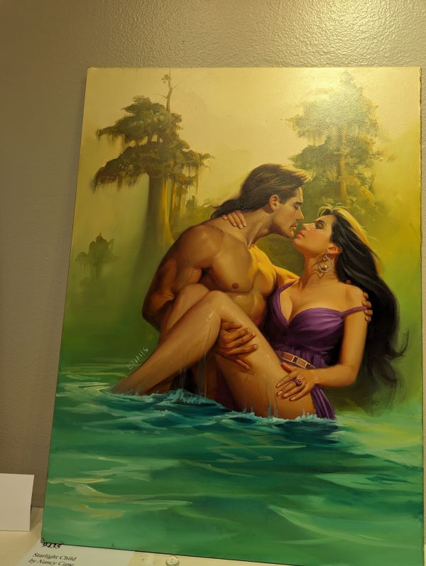 A Long haired John DeSalvo shirtless in some kinda suspicious looking water holding a white woman with long dark hair and a purple gown in a lifeguard carry