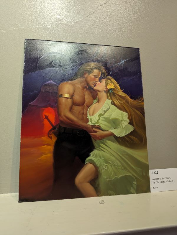 A white man with a mullet and a gold arm band and no shirt obvs stans in front of a tent? maybe? and there's a moon or a space station in the sky, and he's embracing a woman with long gold hair and a green ruffled dress