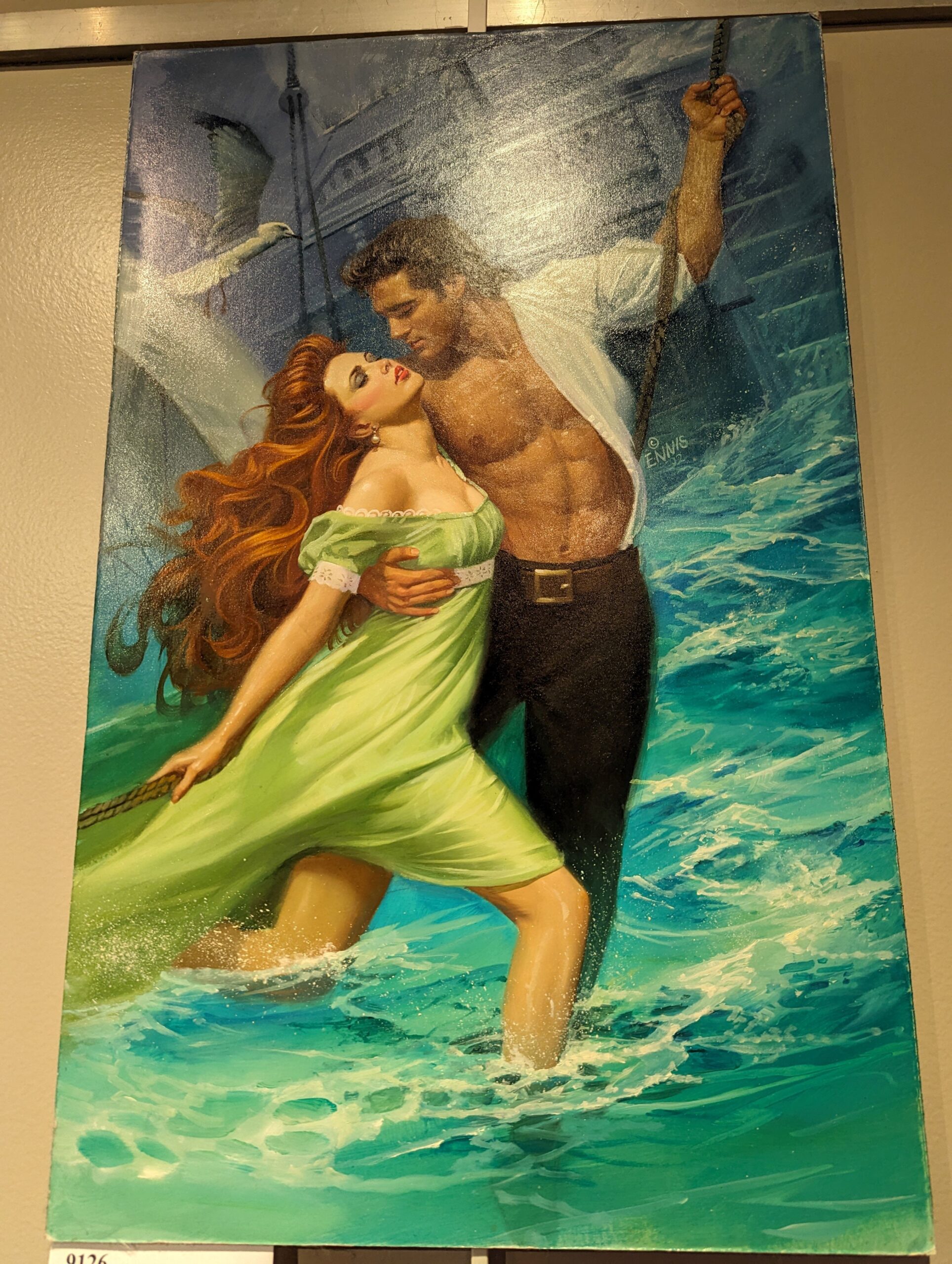 A white redhaired woman in a green gown in the surf up to her calves is embraced by a guy who has his shirt tucked in but still open as he maybe swings from a rope? Dead center are some ABS.