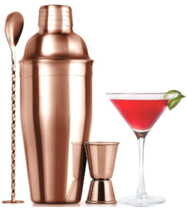 A rose gold drink mixing set with a shaker, long handled spoon, and a two sided cocktail jigger and a recipe book.