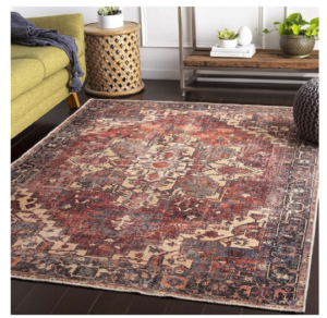 A dark red patterend rug with blue accents on a dark wood floor with a green yellow sofa in the background