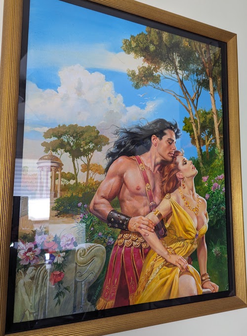 A photograph with some glare sorry of the oil painting for The Lion and the Lark featuring John DeSalvo wearing a hot pink gladiator toga embracing from behind a woman with improbable bazongas wearing a low cut yellow gown. She has red hair and they're posed in a garden with a semi phallic gazebo 