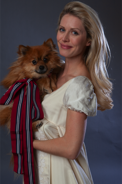 A blonde woman with a white empire gown holds Rocky, who is wearing a big bow!