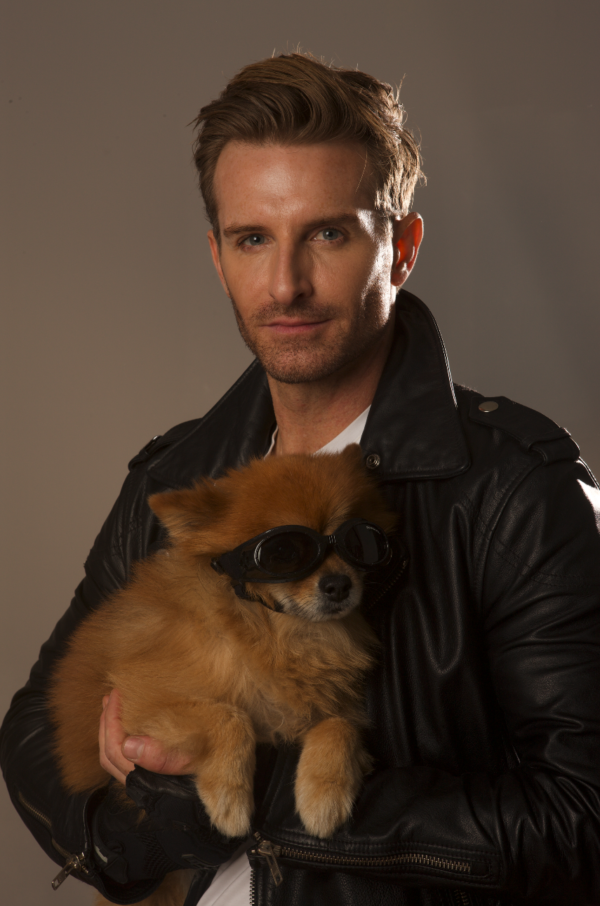 A white dude with a leather jacket holding Rocky, who is wearing a pair of goggles