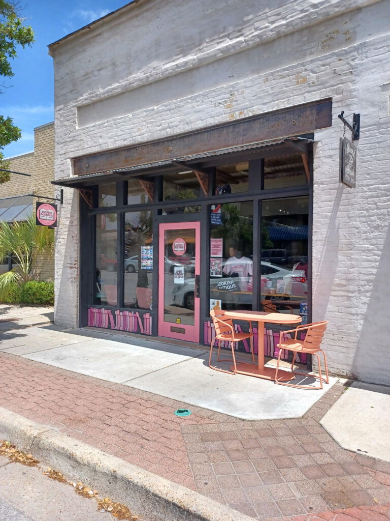 Bookish Boutique storefront. A white stone storefront with large windows and a pink framed door.