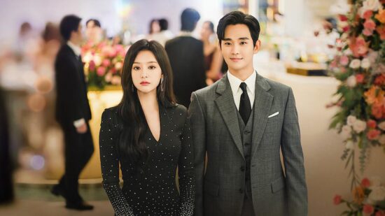 A scene from the film inside the department store. Hae In is wearing a grey suit with a black tie and a smile, while Hyun Woo is wearing a black suit with pearls sewn onto it. He is smiling and she looks miserable 