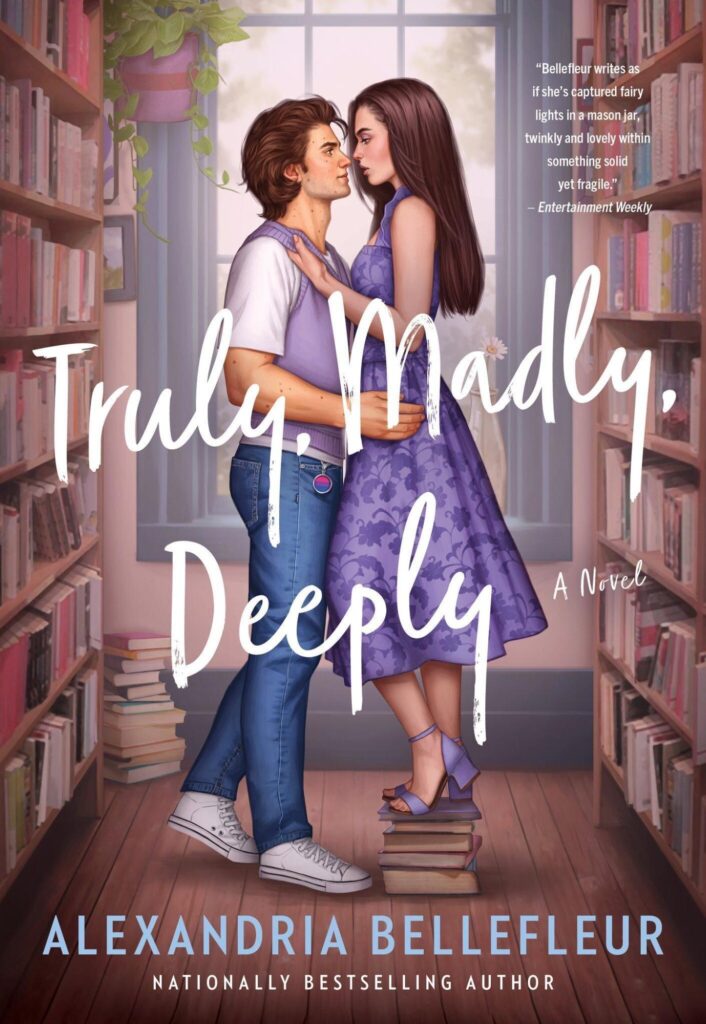 Truly Madly Deeply by Alexandria Bellefleur. An illustration of a man and woman with bookshelves on either side of them. She is standing on a stack of books and is wearing a purple, floral sun dress and matching heels. She has a straight brown hair that falls to the middle of her back. The man is in jeans, white sneakers and white t-shirt, and a purple sweater vest. He has brown, floppy hair. She is slightly taller because of the aforementioned pile of books she is standing on. She is gripping his sweater vest. A window with a hanging plant is behind them and he has a bisexual pride pin hanging from his jeans.