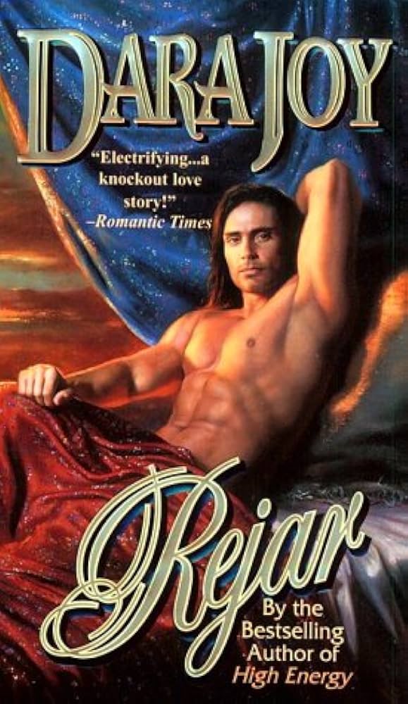 JOhn DeSalvo with long ahir posing on some pillows under a blanket with one arm up and flexed so the focus is his armpit.