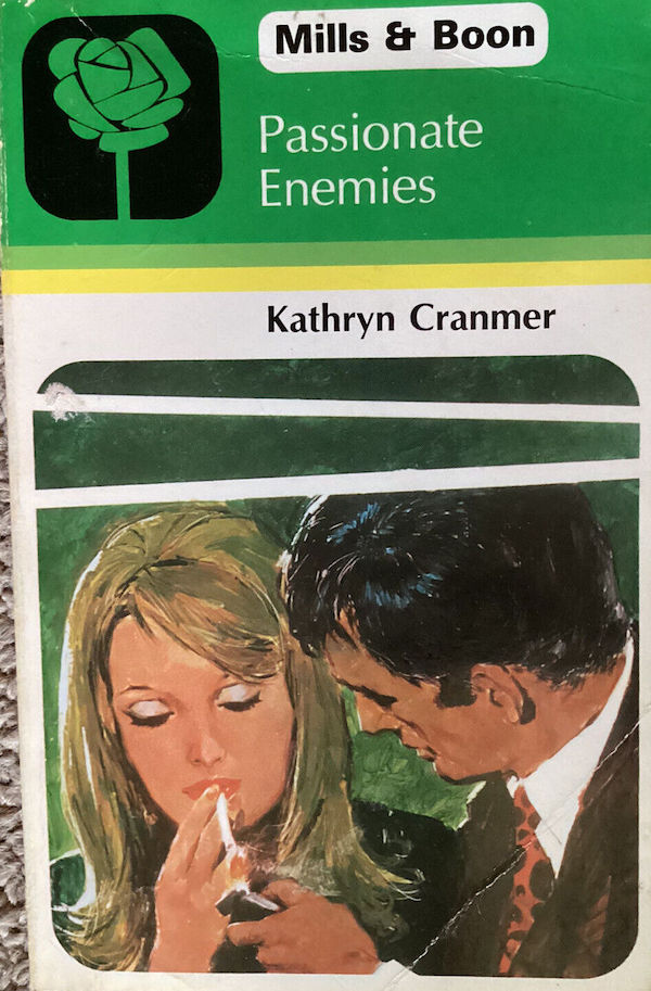 The Mills and boon cover has the green mills and boon logo and header for about a third of the cover and the below that is an illustration of a dark haired man in a suit lighting a blonde woman's cigarette