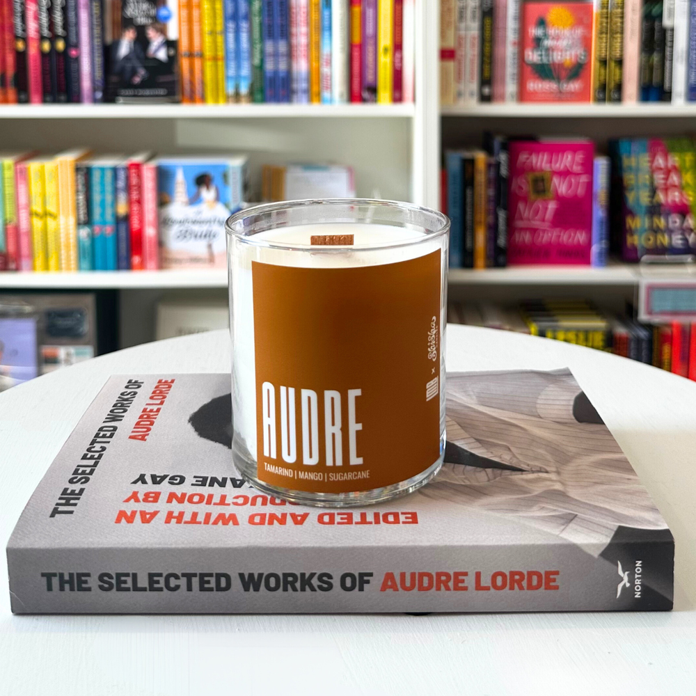 A white candle in a glass jar rests on the book The Selected Works of Audre Lorde. The candle has a burnt orange label with the name Audre in slim, block text. 