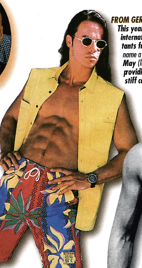This is Andy, and he's wearing a sleeveless yellow vest with a bathing suit flexing his abs with his hands on his hips. The bathing suit has stylized flowers printed on it and one si directly over his crotch