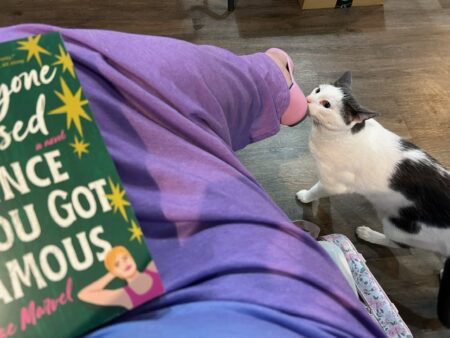 A shot of my lap. I'm seated with one leg crossed over the other, the book in my lap. A gray and white cat sniffs my shoe.