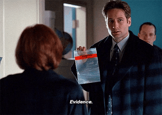 Mulder holds up a bag and runs a finger under the EVIDENCE label while mouthing the word EVIDENCE