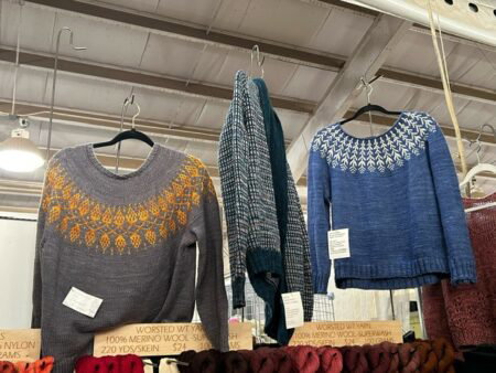 Two yoke sweaters hang side by side. One is orange and gray and the other blue and white