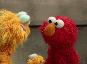 Elmo looks away from a rock named Rocco and stares at the camera like what the hell is happening
