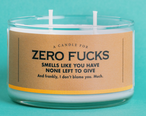 A candle in a round glass jar with two wicks. The label says A candle for Zero Fucks. Smells like you have none left to give. And frankly, I don't blame you, much