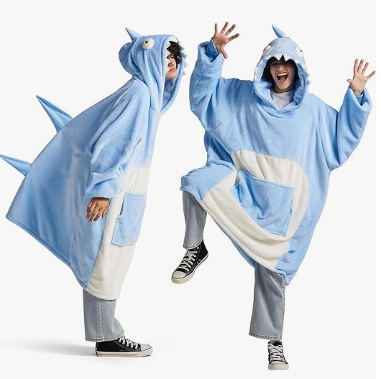 A white dude in converse and jeans is wearing a giant shark hoodie made of fluffy fleece material with teeth, fins, and a big blue pocket on a white belly patch. In one image the person is standing to the side, and in the other the person is lifting one leg and dancing 