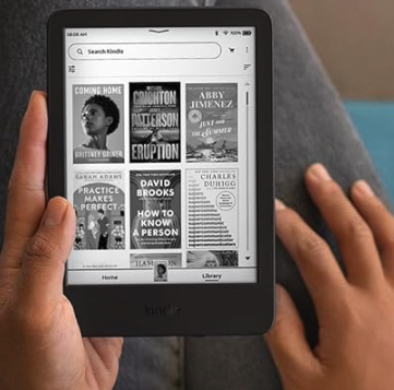 A Kindle held in a persons' hands with black denim behind 