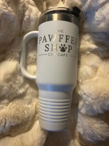 A white insulated tumbler with a handle with the Pawffee Shop logo