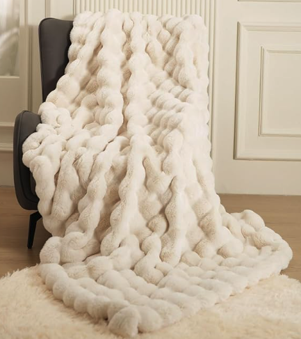 A faux rabbit fur blanket in cream draped over a chair 