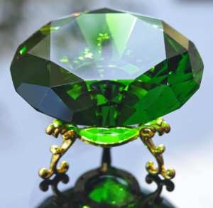 A close up of the green crystal on its stand from above against a reflective backdrop