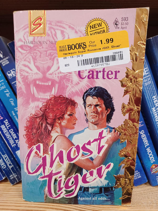 Ghost Tiger by someone named Carter. the sticker is over the name. Janice! Janice Carter. Thanks, Google. Anyway, there's a woman with curly hair in a ponytail and I think her hair is full on fuchsia. She's standing facing the side with her hand resting on the shoulder of a man facing the reader. He's looking off to the side, but his MULLET is Excellent. There is gold leaf printing of maybe daffodils up the side, and in the background is a pink washed image of a snarling tiger. 